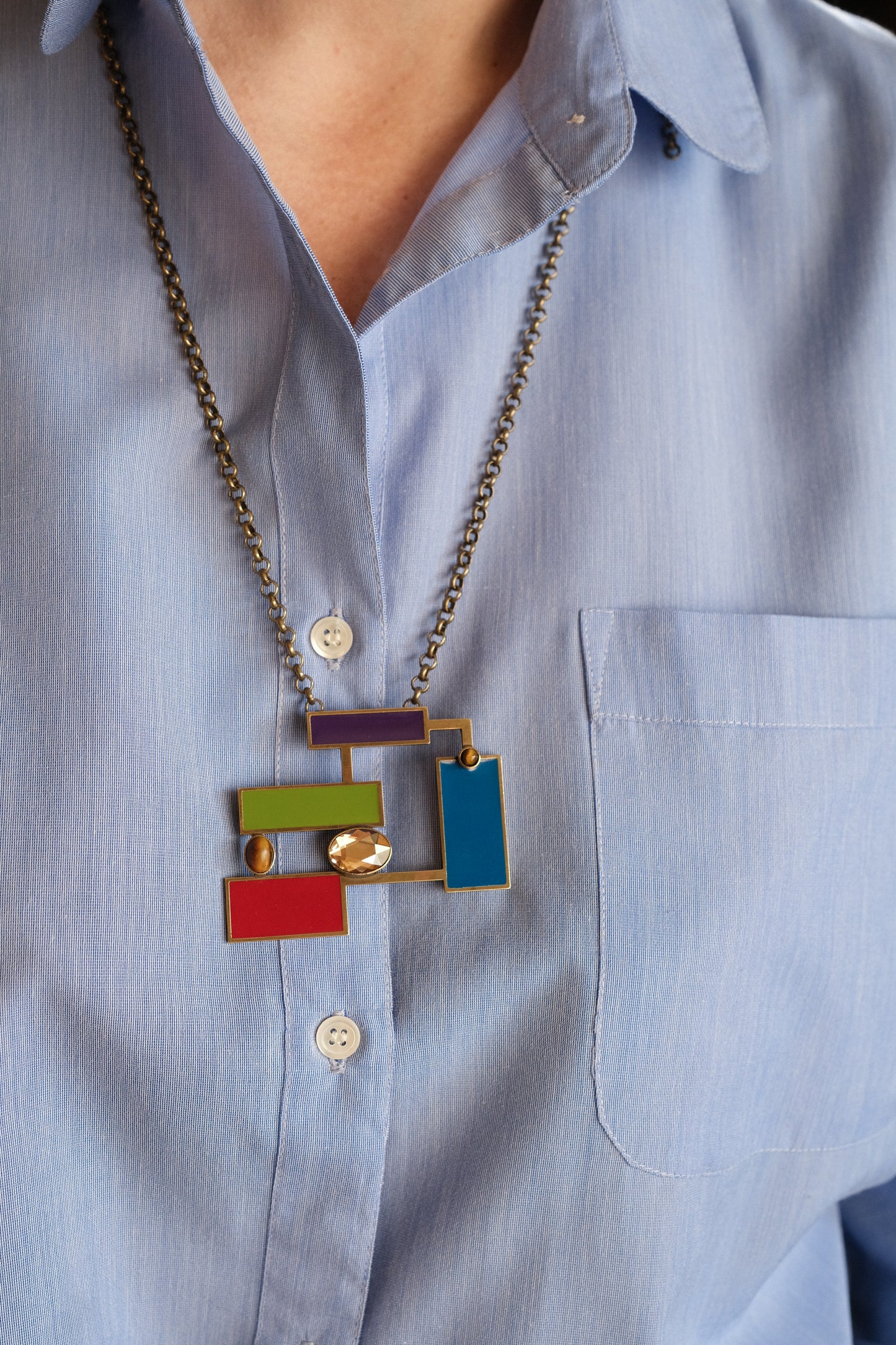 Suzanne Tiger's eye brooch pendant showcasing Art Deco designs with colorful enamels, worn over a blue shirt.