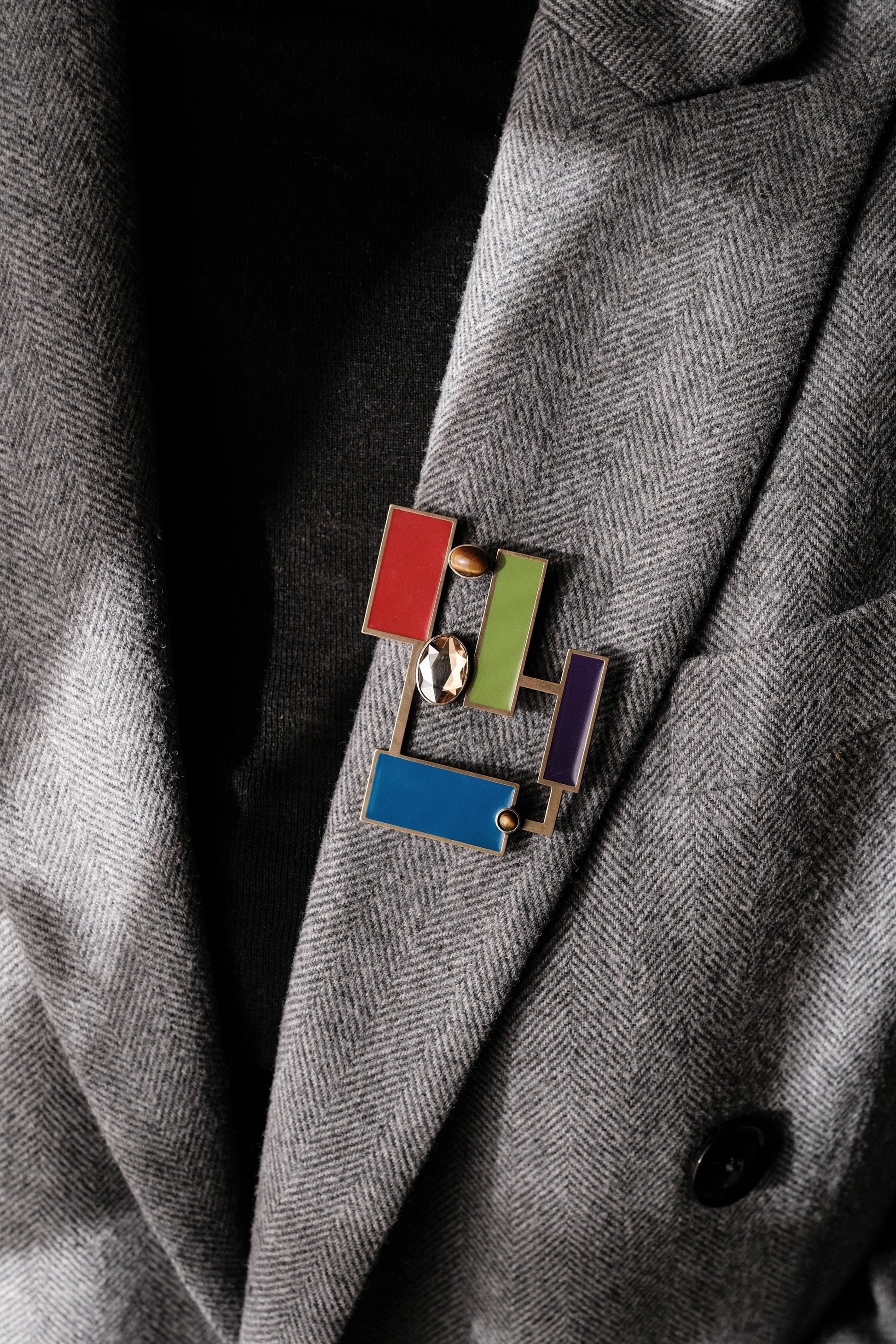 Suzanne Tiger's eye brooch pendant featuring colorful geometric enamels on a stylish blazer.